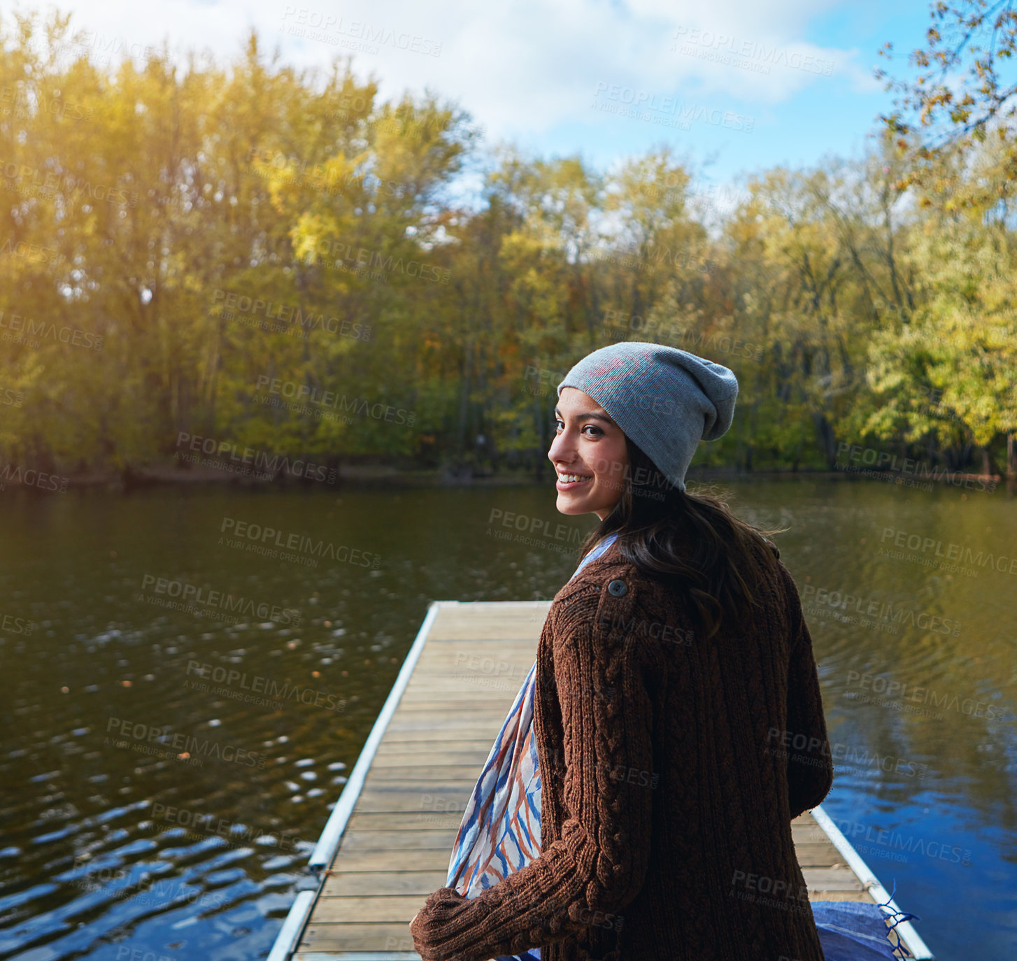 Buy stock photo Shot of a happy young woman standing on a pier next to a lake