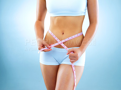 Buy stock photo Cropped studio shot of a fit young woman measuring her waist against a blue background