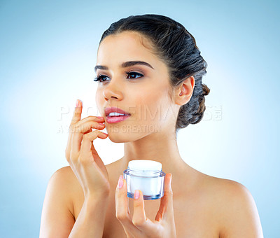 Buy stock photo Studio shot of a beautiful young woman applying moisturizer to her face against a blue background