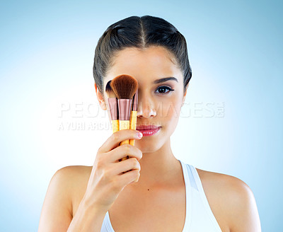 Buy stock photo Cropped portrait of a beautiful young woman holding up makeup brushes against a blue background