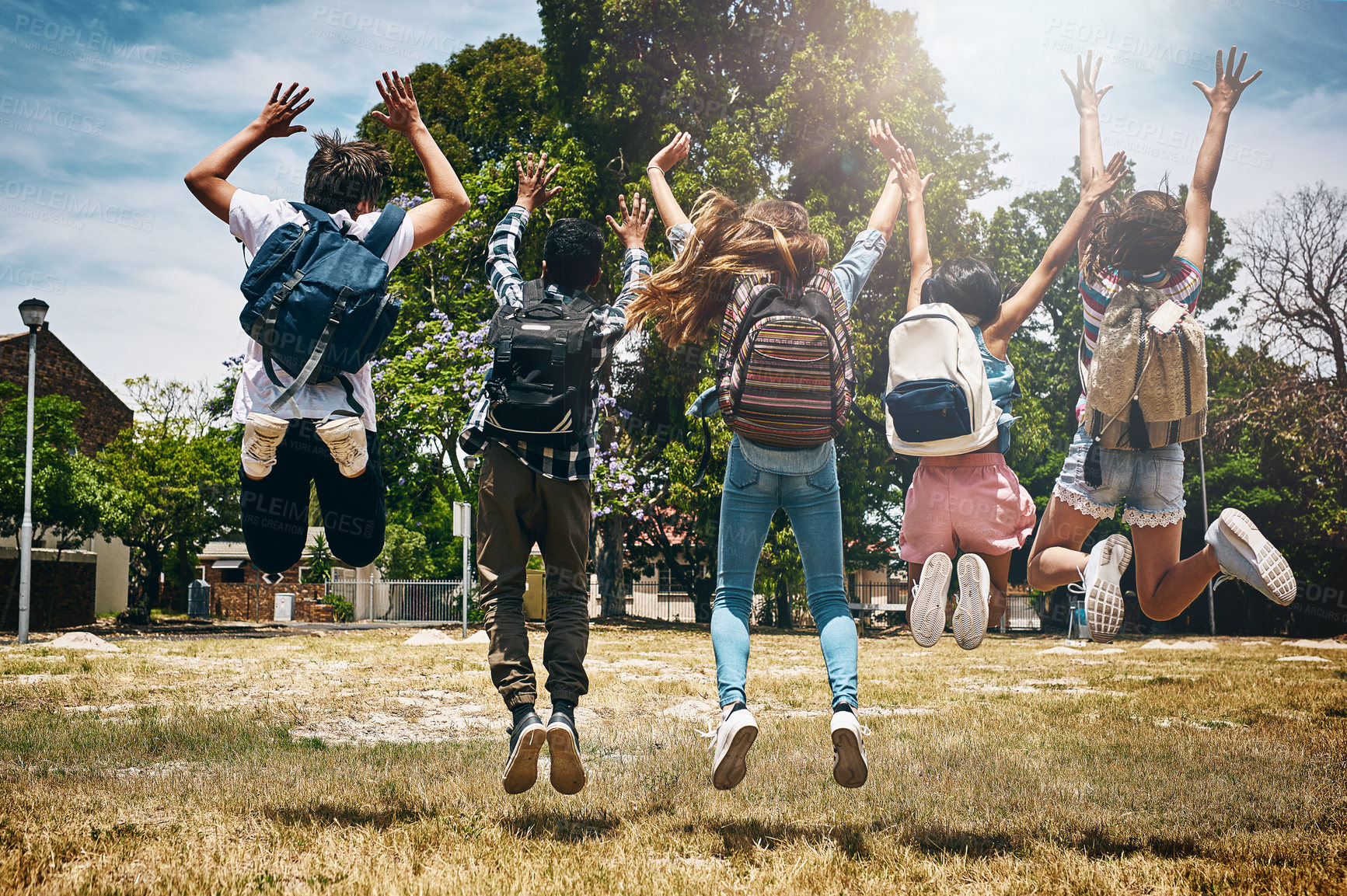 Buy stock photo Rearview shot of a group of unidentifiable schoolchildren jumping in the park