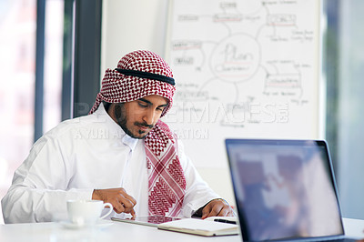 Buy stock photo Shot of a young muslim businessman using a digital tablet at his work desk
