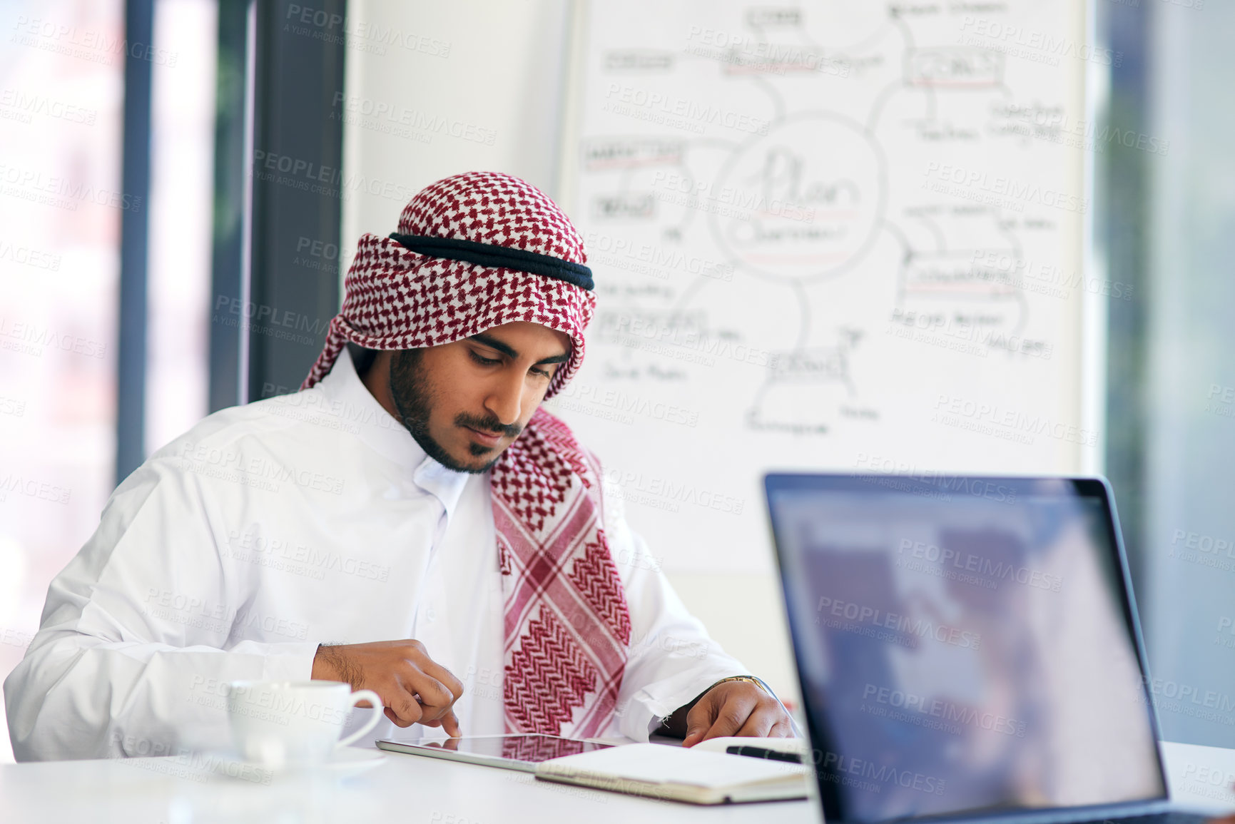 Buy stock photo Shot of a young muslim businessman using a digital tablet at his work desk
