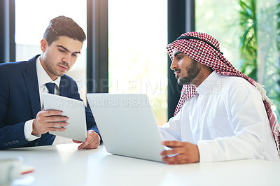 Buy stock photo Shot of a young muslim businessman using a laptop and digital tablet with his colleague at work
