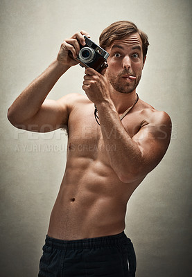 Buy stock photo Studio shot of a shirtless young man taking photos with a vintage camera while making funny faces