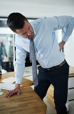 Buy stock photo Shot of a young businessman experiencing back pain at work