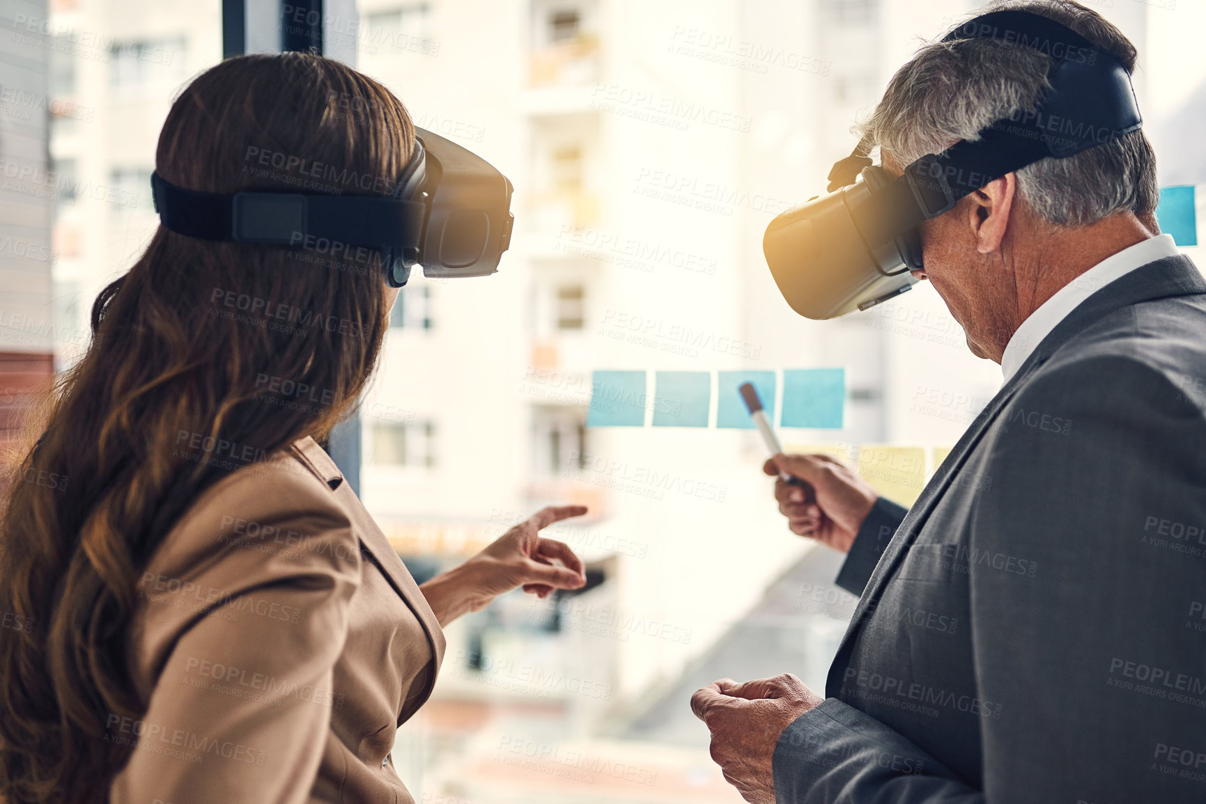 Buy stock photo Shot of two businesspeople wearing VR headsets while working with notes on a glass wall in an office