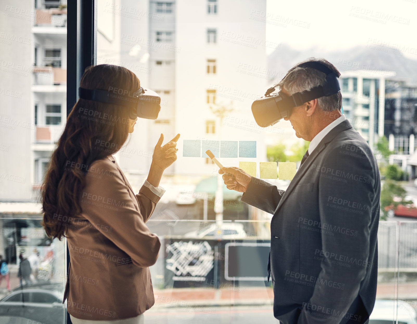 Buy stock photo Shot of two businesspeople wearing VR headsets while working with notes on a glass wall in an office