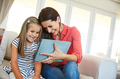 Buy stock photo Shot of a mother and her young daughter sitting together in the living room at home using a digital tablet