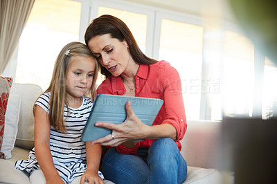Buy stock photo Shot of a mother and her young daughter sitting together in the living room at home using a digital tablet