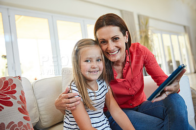Buy stock photo Portrait of a mother and  her young daughter sitting together in the living room at home using a digital tablet