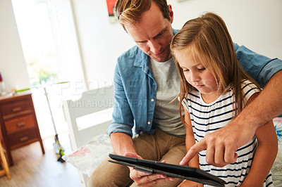 Buy stock photo Shot of a father and his young daughter sitting together in the living room at home using a digital tablet