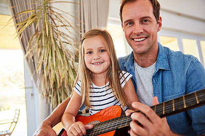 Buy stock photo Portrait of a father and his young daughter sitting together in the living room at home playing guitar