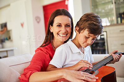 Buy stock photo Portrait of a mother and her young son sitting together in the living room at home playing guitar