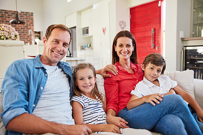 Buy stock photo Portrait of smiling parents sitting with their young son and daughter on their living room sofa at home