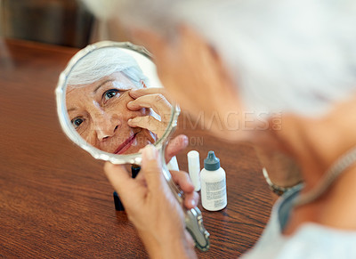 Buy stock photo Shot of a senior woman using a hand mirror to look at her skin at home