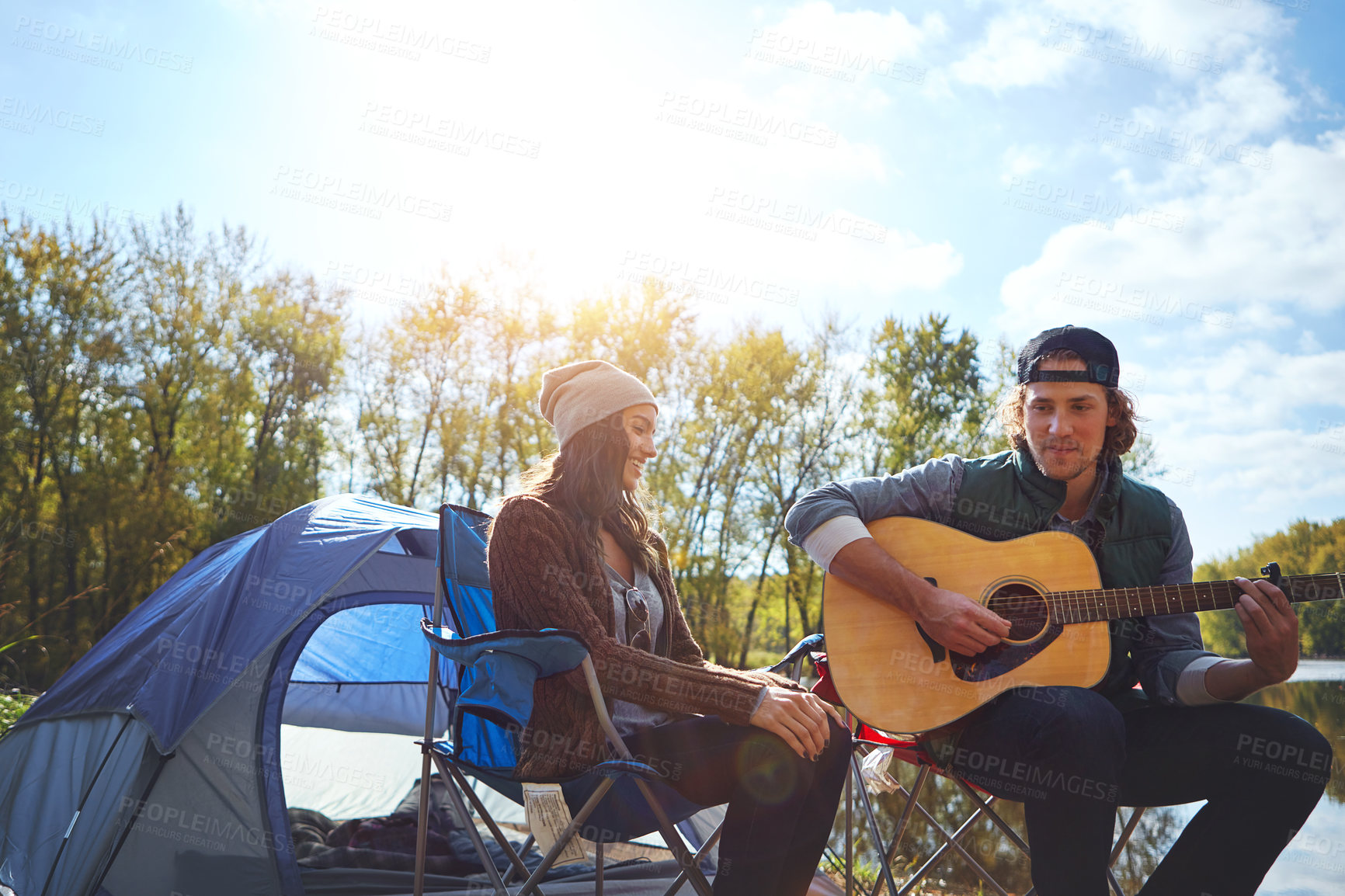 Buy stock photo Shot of a young man playing his girlfriend a song on his guitar while out camping