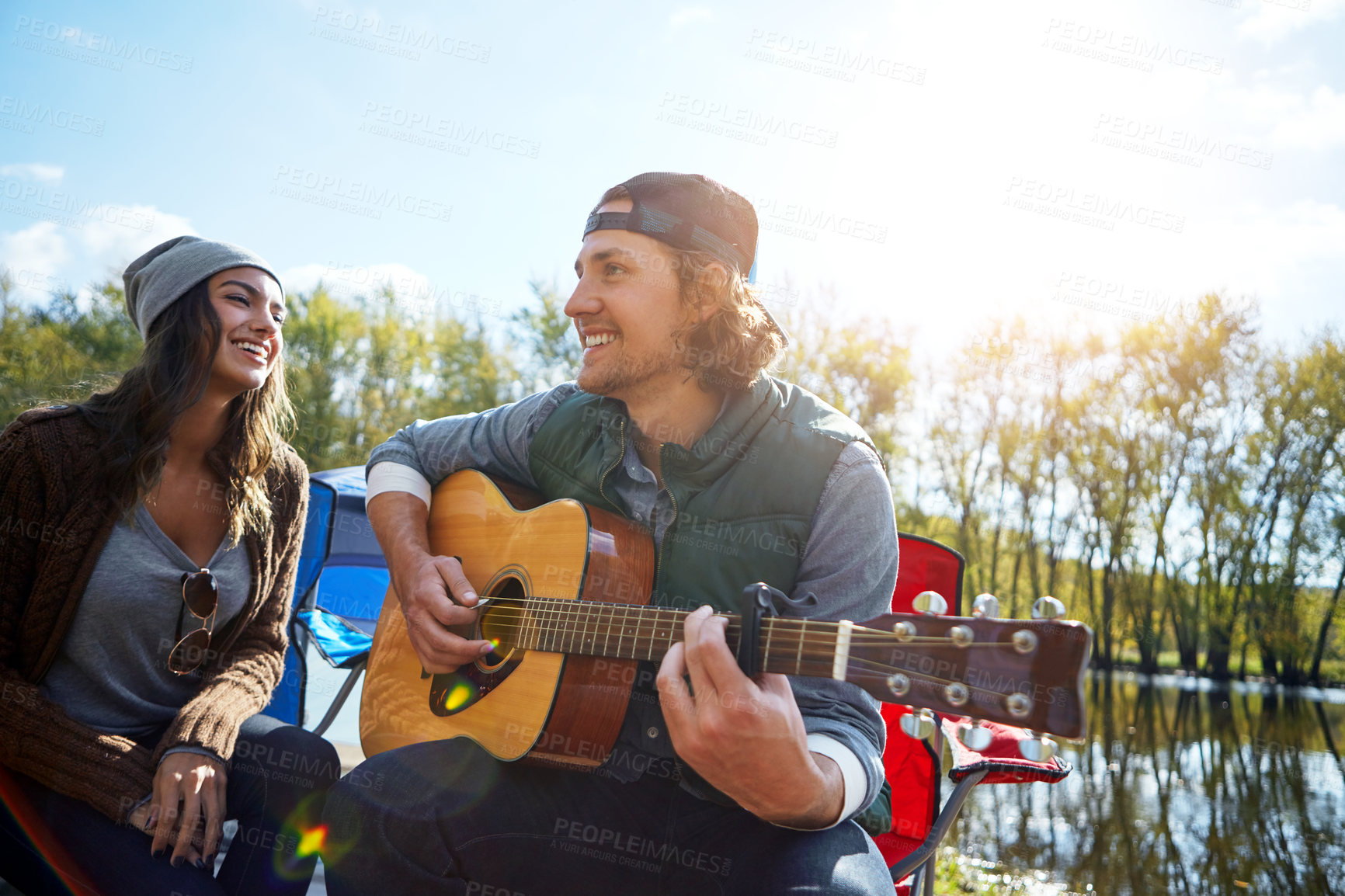 Buy stock photo Shot of a young man playing his girlfriend a song on his guitar while out camping