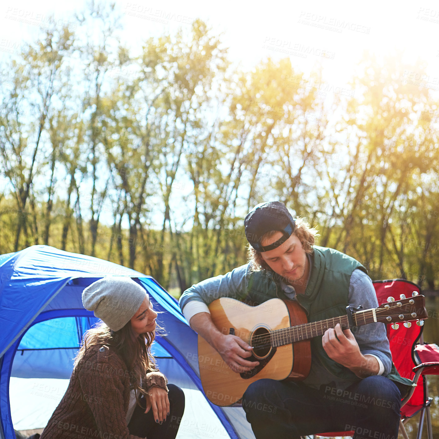 Buy stock photo Shot of a young man playing his girlfriend a song on his guitar while out camping