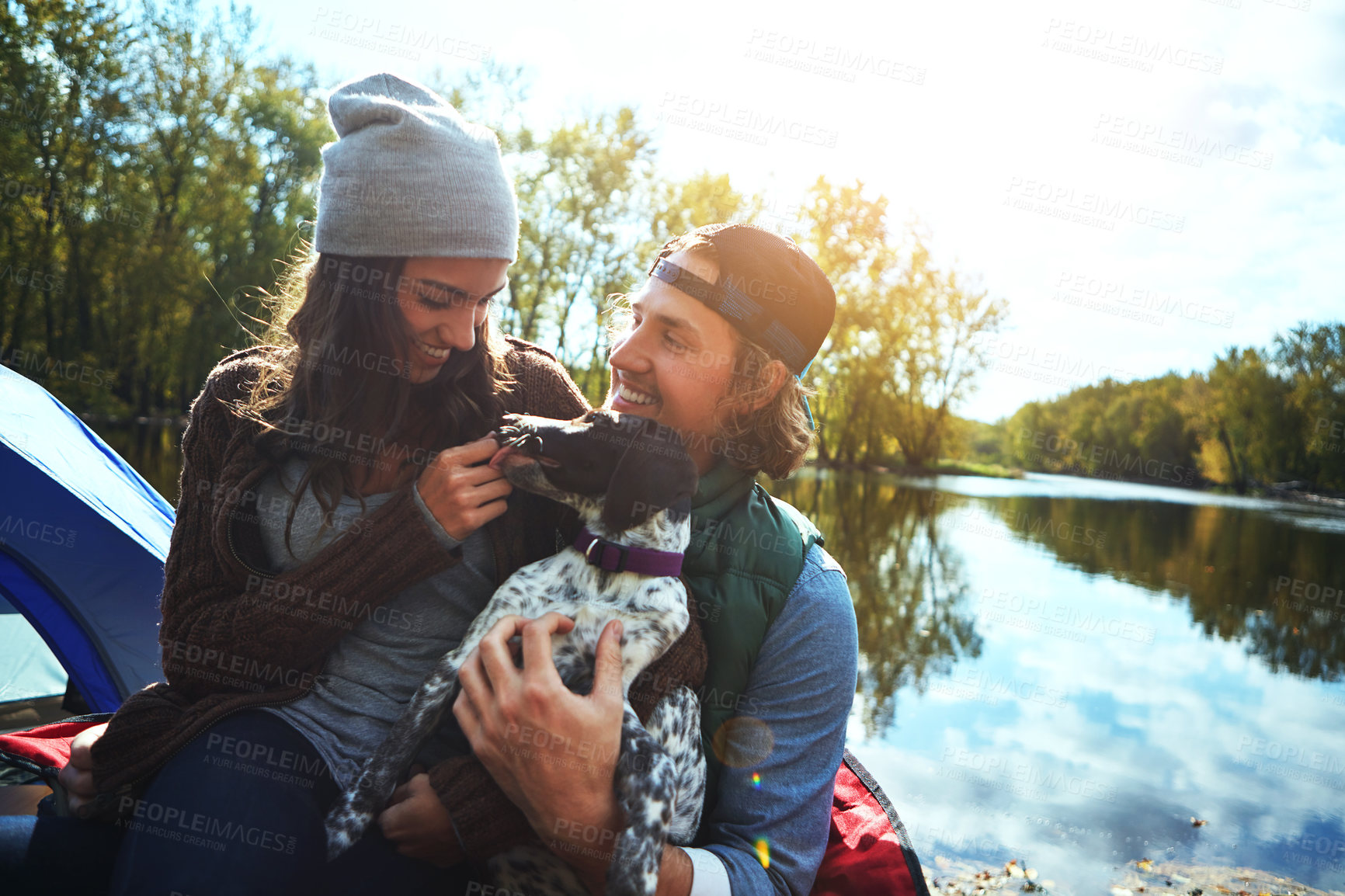 Buy stock photo Camping, couple and dog for adventure with love of park in nature lake, sunshine and smile, travel or animal holiday. Happy, woman and man with puppy pet for care, hug or relax in summer journey