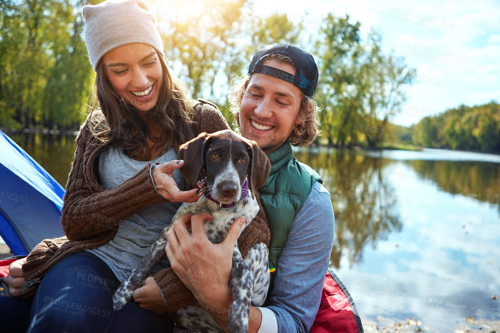 Buy stock photo Dog, couple and love in nature for camping in forest, sunshine and bond, smile and support of animal on adventure time. Happy, woman and man with puppy pet for care, hug or relax in summer journey