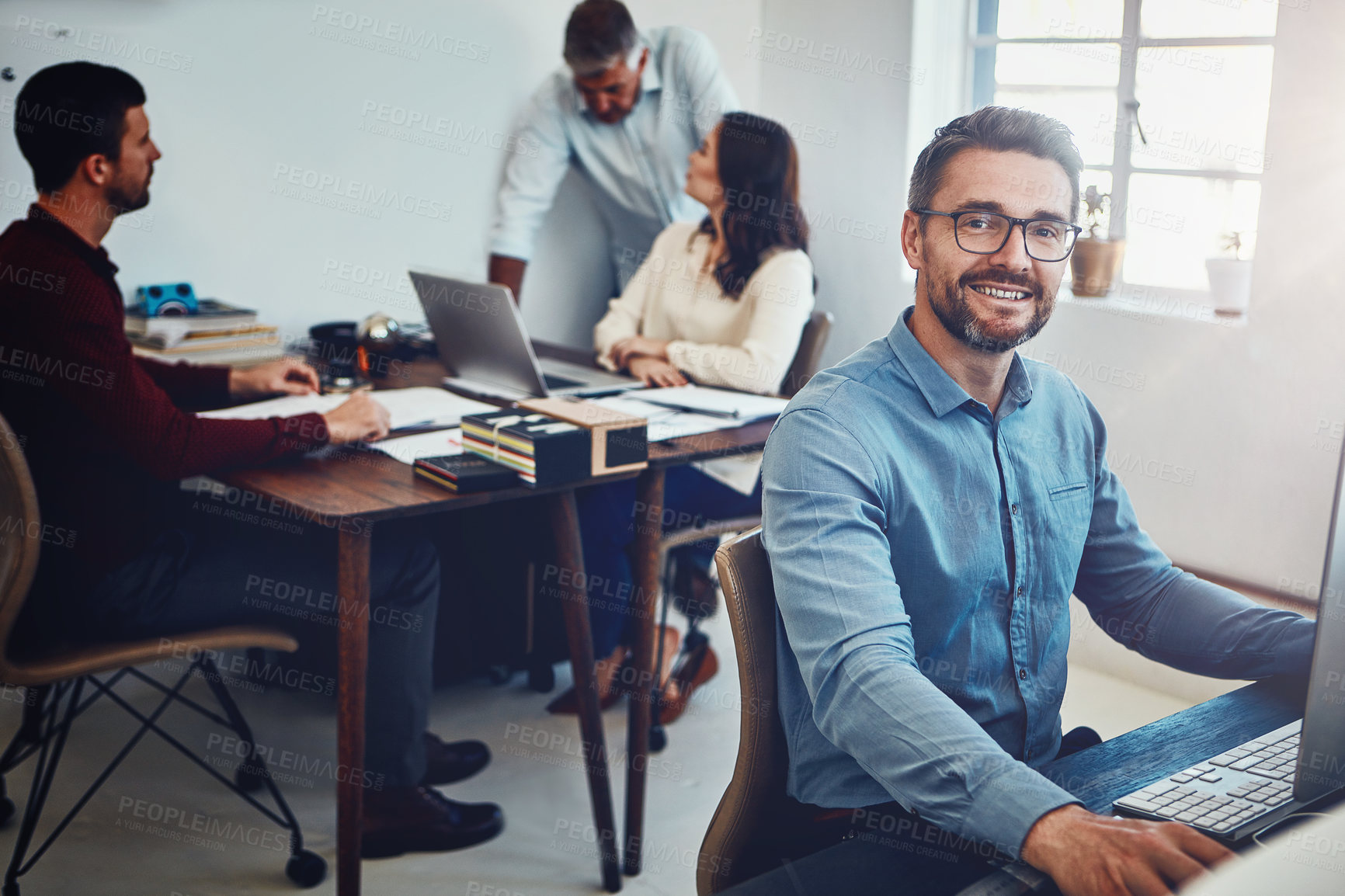 Buy stock photo Portrait of a mature man working in the office with his colleagues in the background