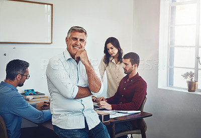 Buy stock photo Portrait of a mature man sitting on a desk in the office which his colleagues are working on