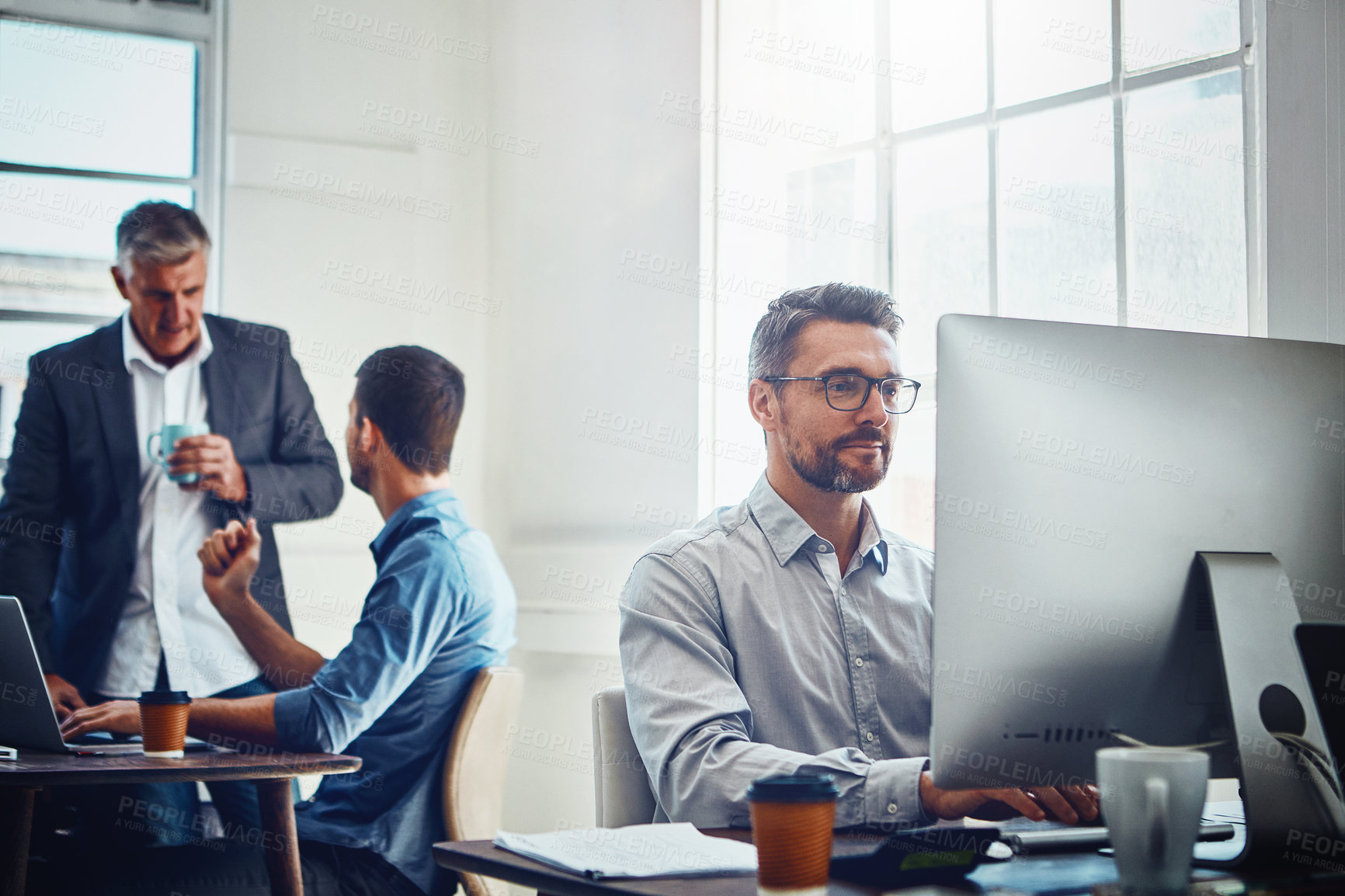 Buy stock photo Computer, work and businessman with his colleagues in the background talking, speaking and planning. Pc, success and professional male employee working on a corporate company report in the office.