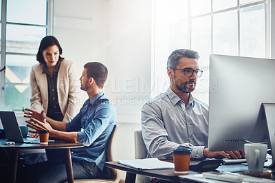 Buy stock photo Shot of mature businessman using a computer at work with his colleagues in the background