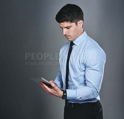 Buy stock photo Studio shot of a young businessman using a digital tablet against a grey background