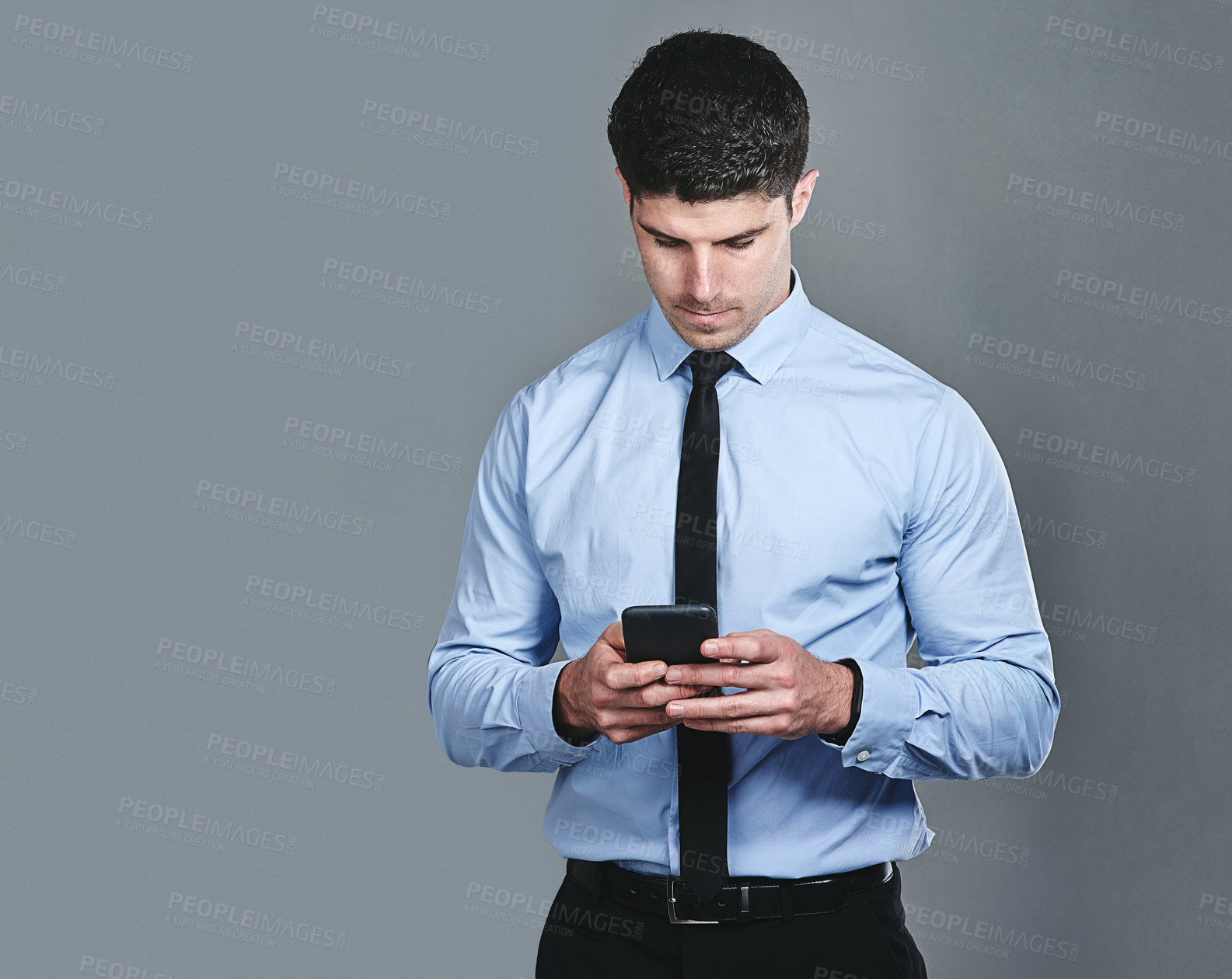 Buy stock photo Studio shot of a young businessman texting on a cellphone against a grey background