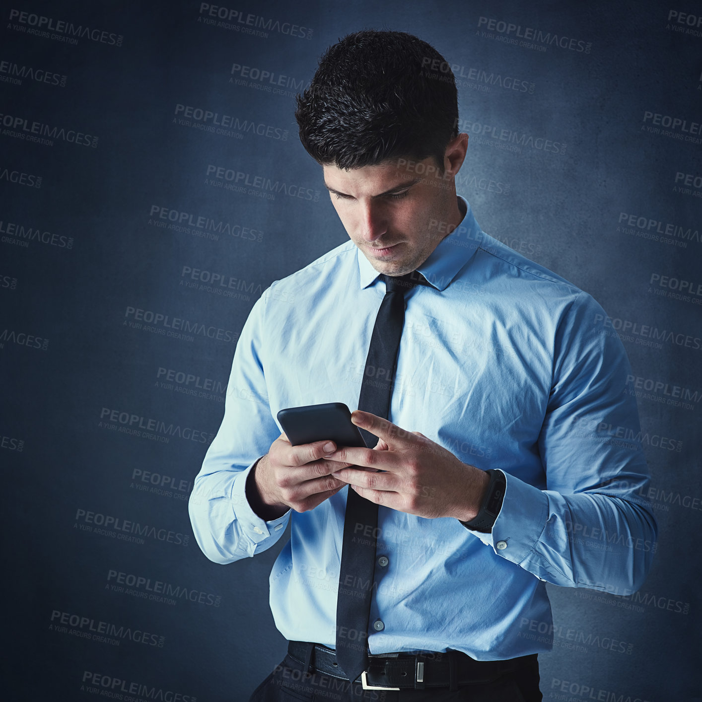 Buy stock photo Studio shot of a young businessman texting on a cellphone against a dark background