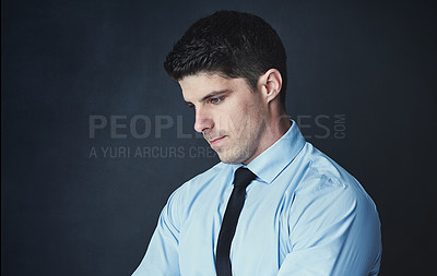 Buy stock photo Studio shot of a young businessman looking thoughtful against a dark background