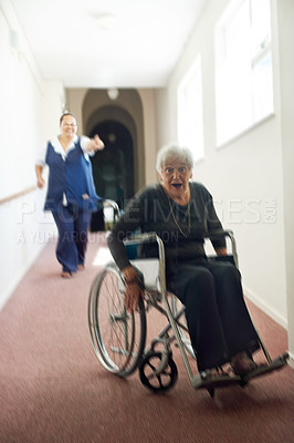 Buy stock photo Shot of a mischievous senior woman using her wheelchair to run away form her nurse in an old age home