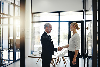 Buy stock photo Cropped shot of two businesspeople shaking hands while standing in the office