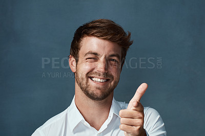 Buy stock photo Studio portrait of a handsome young man showing thumbs up against a dark background