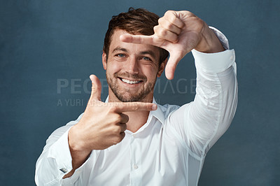 Buy stock photo Studio portrait of a handsome young man framing with his fingers against a dark background