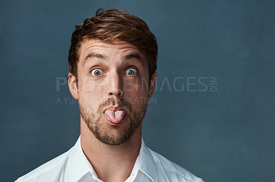 Buy stock photo Studio portrait of a handsome young man sticking his tongue out against a dark background