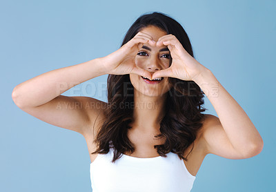 Buy stock photo Studio shot of an attractive young woman making a heart shape with her hands against a blue background