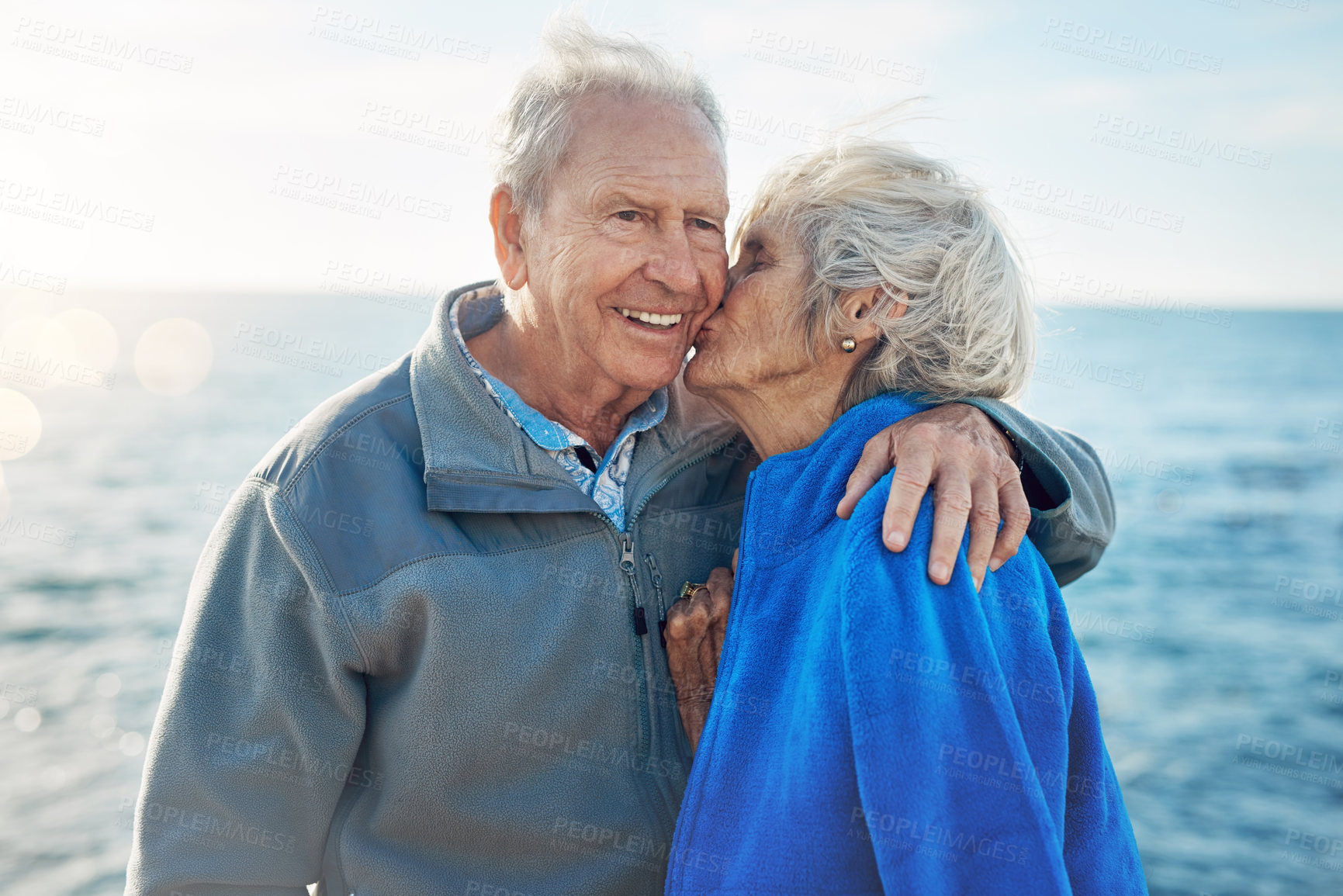 Buy stock photo Senior couple, people and cheek kiss in ocean with support, love and affection for break in Canada. Relationship, date and happy or smile for retirement, holiday and adventure or trip as soulmate