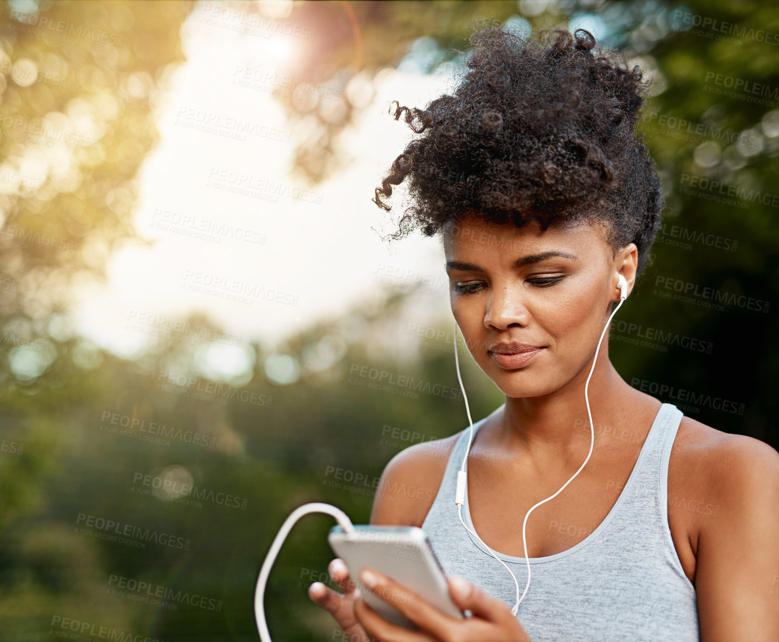 Buy stock photo Shot of a young woman listening to music on her phone while out for a run