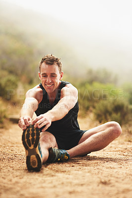 Buy stock photo Shot of a sporty young man stretching before a run outside