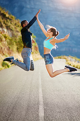 Buy stock photo Shot of a sporty young couple high fiving each other in midair outside