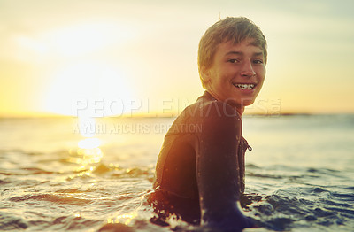 Buy stock photo Portrait of a young boy in a wetsuit sitting on his surfboard in the ocean
