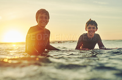 Buy stock photo Portrait of two young brothers sitting on their surfboards in the ocean
