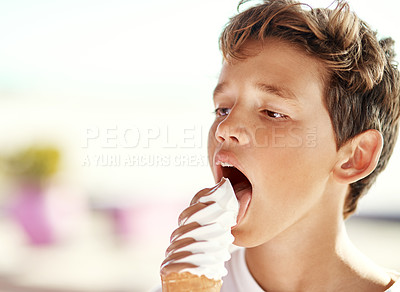 Buy stock photo Shot of a cheerful little boy eating a big ice-cream on his own at the beach