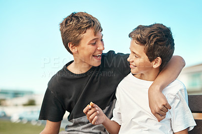 Buy stock photo Shot of two happy brothers sitting on a bench by the beach together