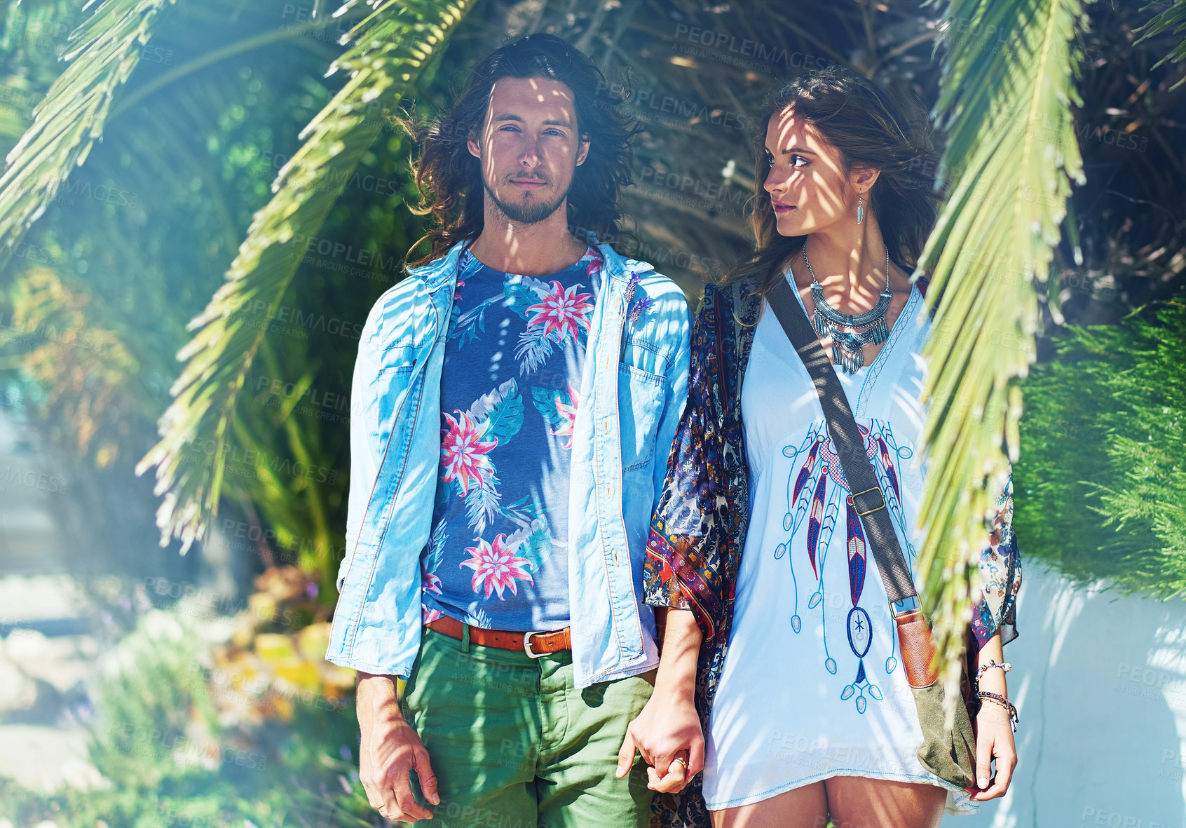 Buy stock photo Shot of a young couple standing hand-in-hand outside under a palm tree