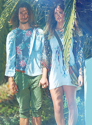 Buy stock photo Shot of a young couple standing hand-in-hand outside under a palm tree