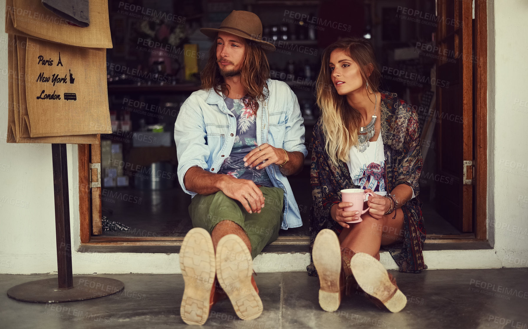 Buy stock photo Shot of an affectionate young couple sitting in the doorway of a roadside shop